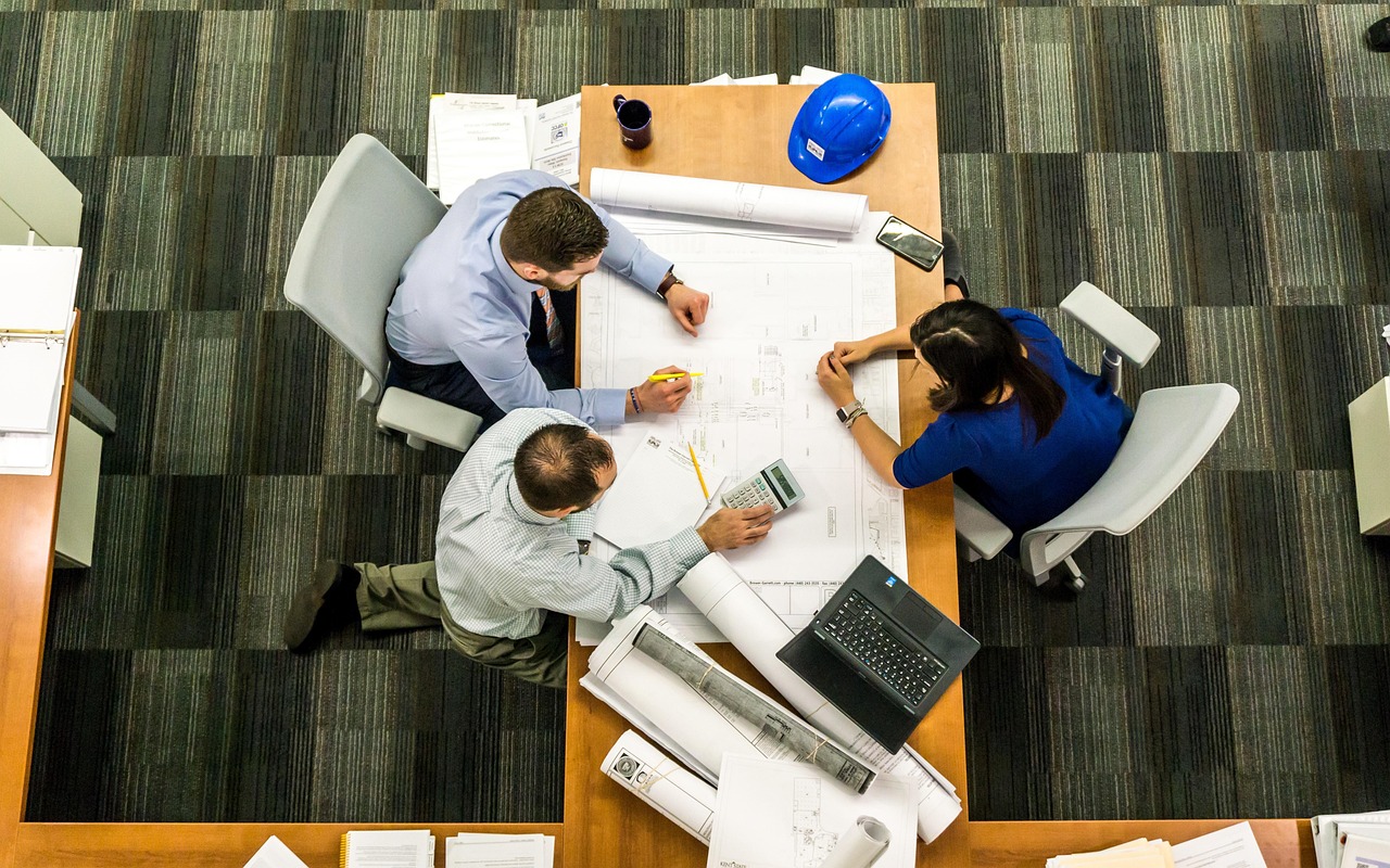 A trades business owner reviewing documents and plans with a broker at a meeting table.